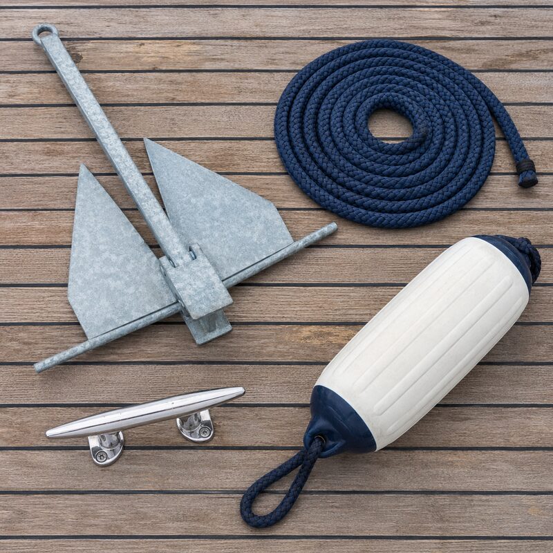 Galvanized anchor, navy dock line, cleat and fender on a wooden deck